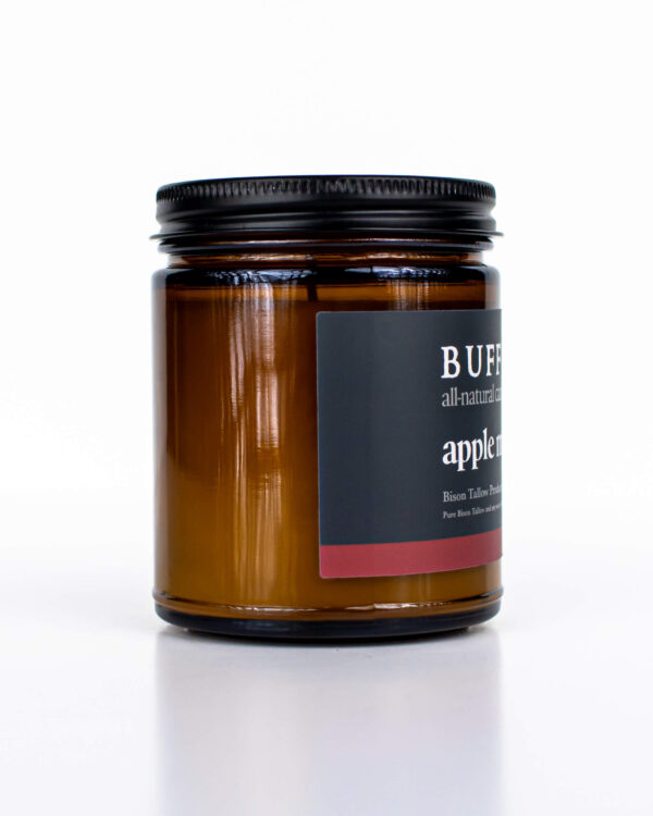 Amber glass all-natural candle with black lid and label featuring the Apple Moonshine fragrance and the Buff Bar Bison illustration. The candle is on a white background.