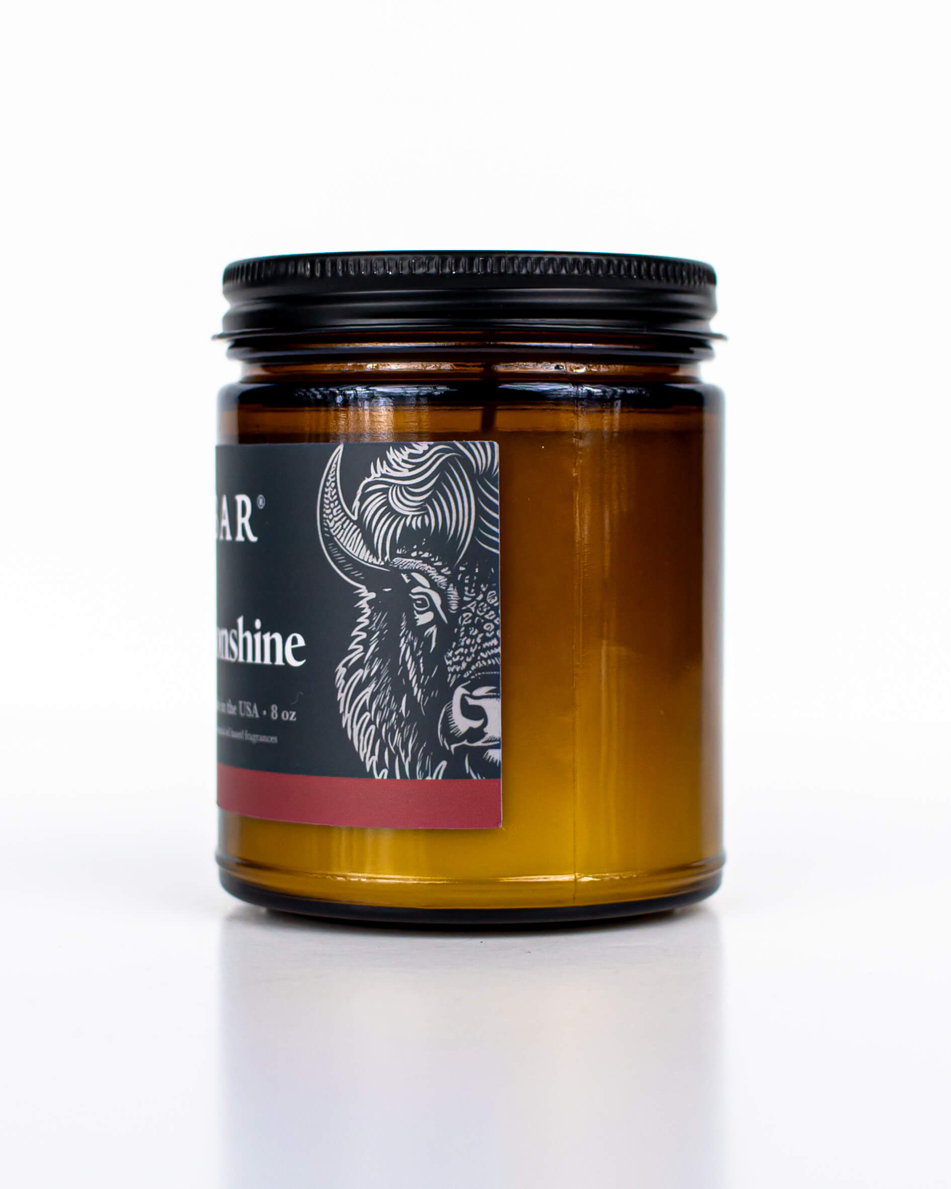 Amber glass all-natural candle with black lid and label featuring the Apple Moonshine fragrance and the Buff Bar Bison illustration. The candle is on a white background.