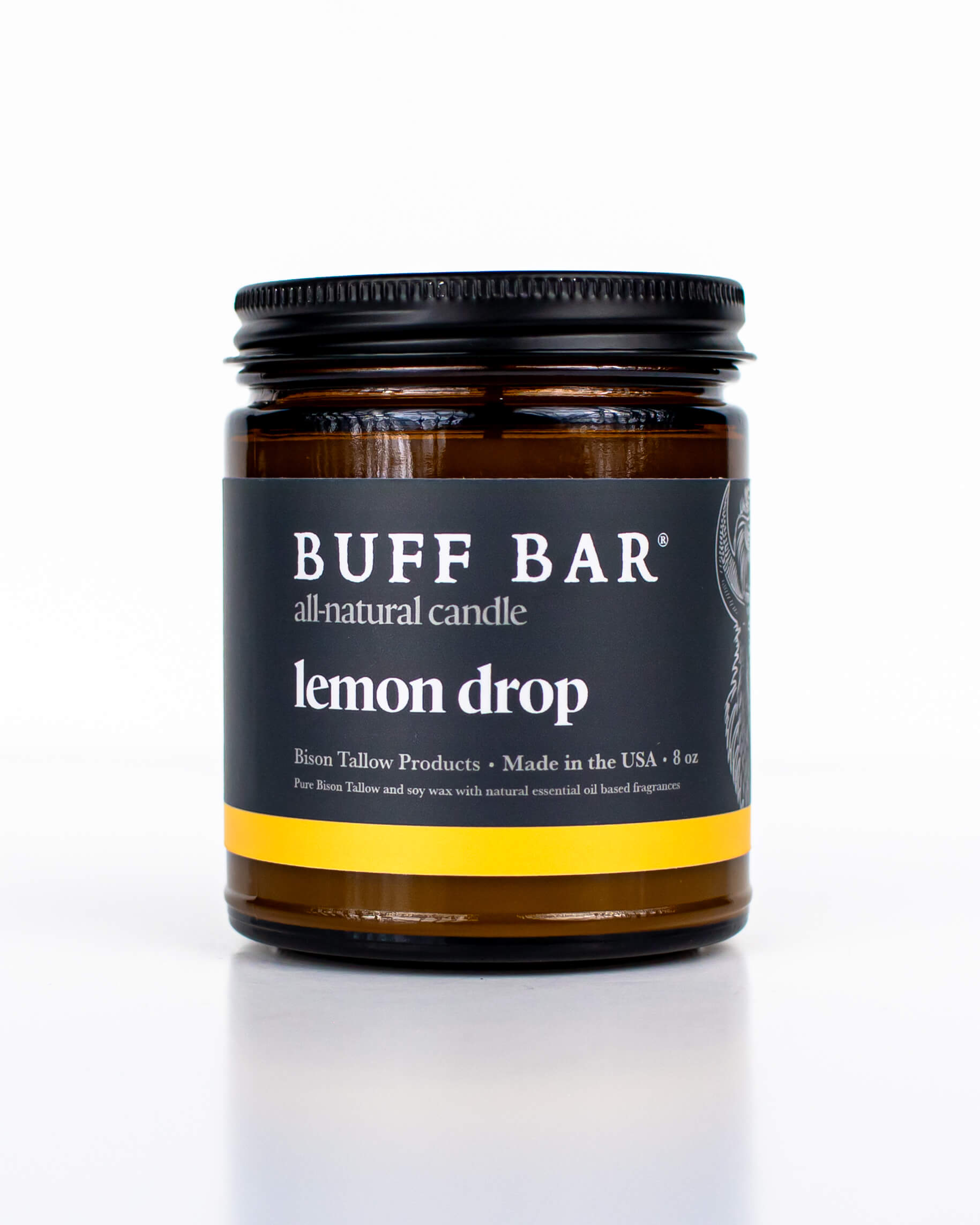 Buff Bar All-natural candle in a amber glass with black lid and label featuring the Lemon Drop fragrance and the Buff Bar Bison illustration. The candle is on a white background.