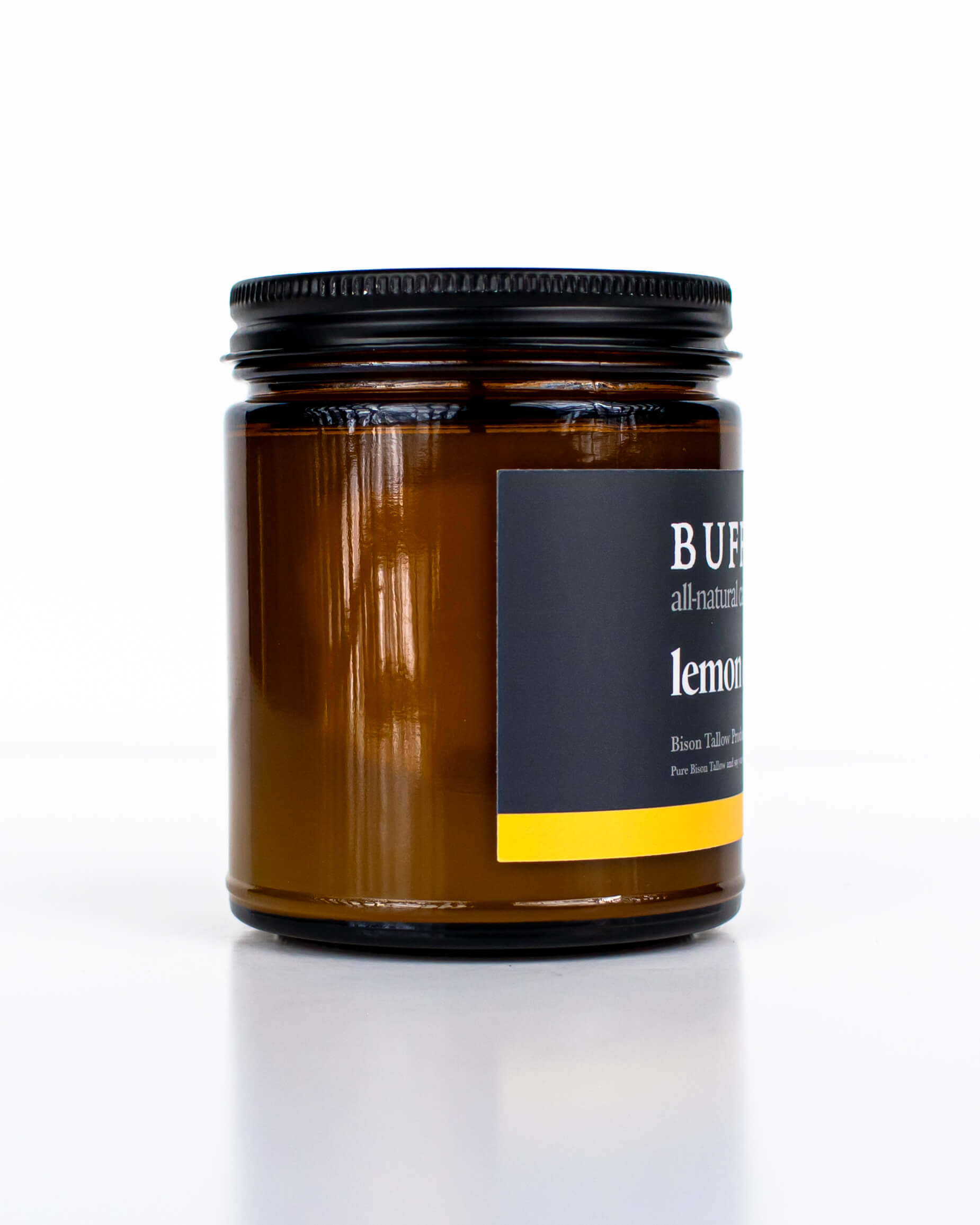 Buff Bar All-natural candle in a amber glass with black lid and label featuring the Lemon Drop fragrance and the Buff Bar Bison illustration. The candle is on a white background.