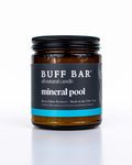 Buff Bar All-natural candle in a amber glass with black lid and label featuring the Mineral Pool fragrance and the Buff Bar Bison illustration. The candle is on a white background.