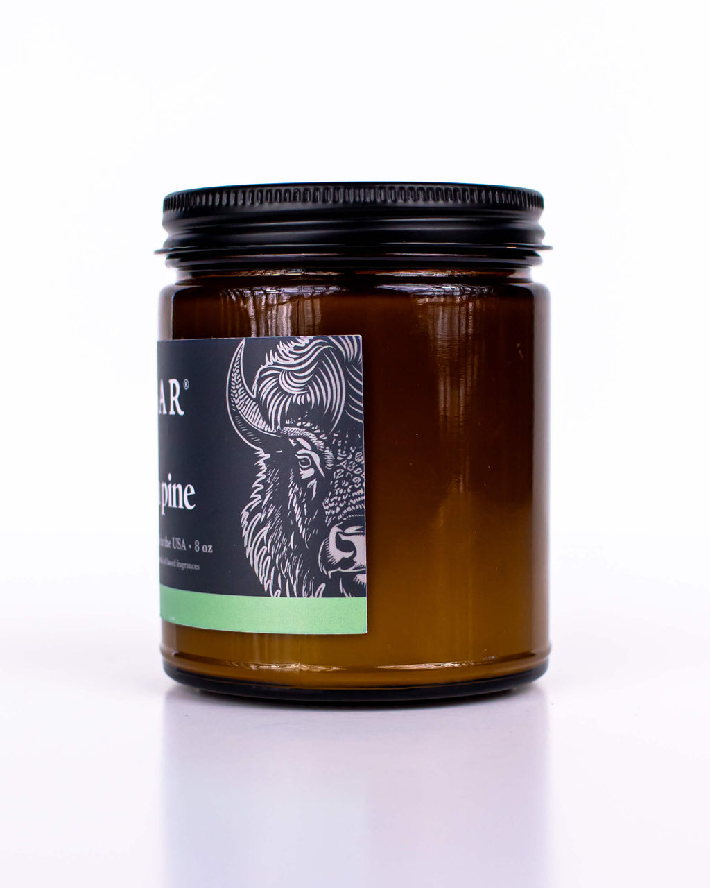 Buff Bar All-natural candle in a amber glass with black lid and label featuring the Ponderosa Pine fragrance and the Buff Bar Bison illustration. The candle is on a white background.